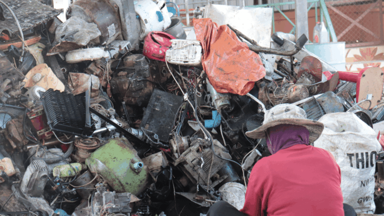 një punëtor i ulur para një grumbulli të madh mbeturinash elektronike plastike