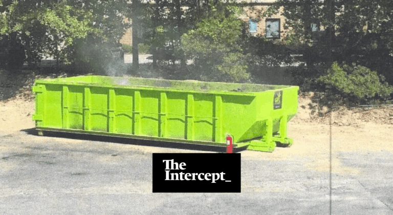 A large, bright green dumpster sits on a paved area near trees and a building. Light smoke rises from inside the dumpster. The Intercept logo is overlaid at the bottom center of the image.