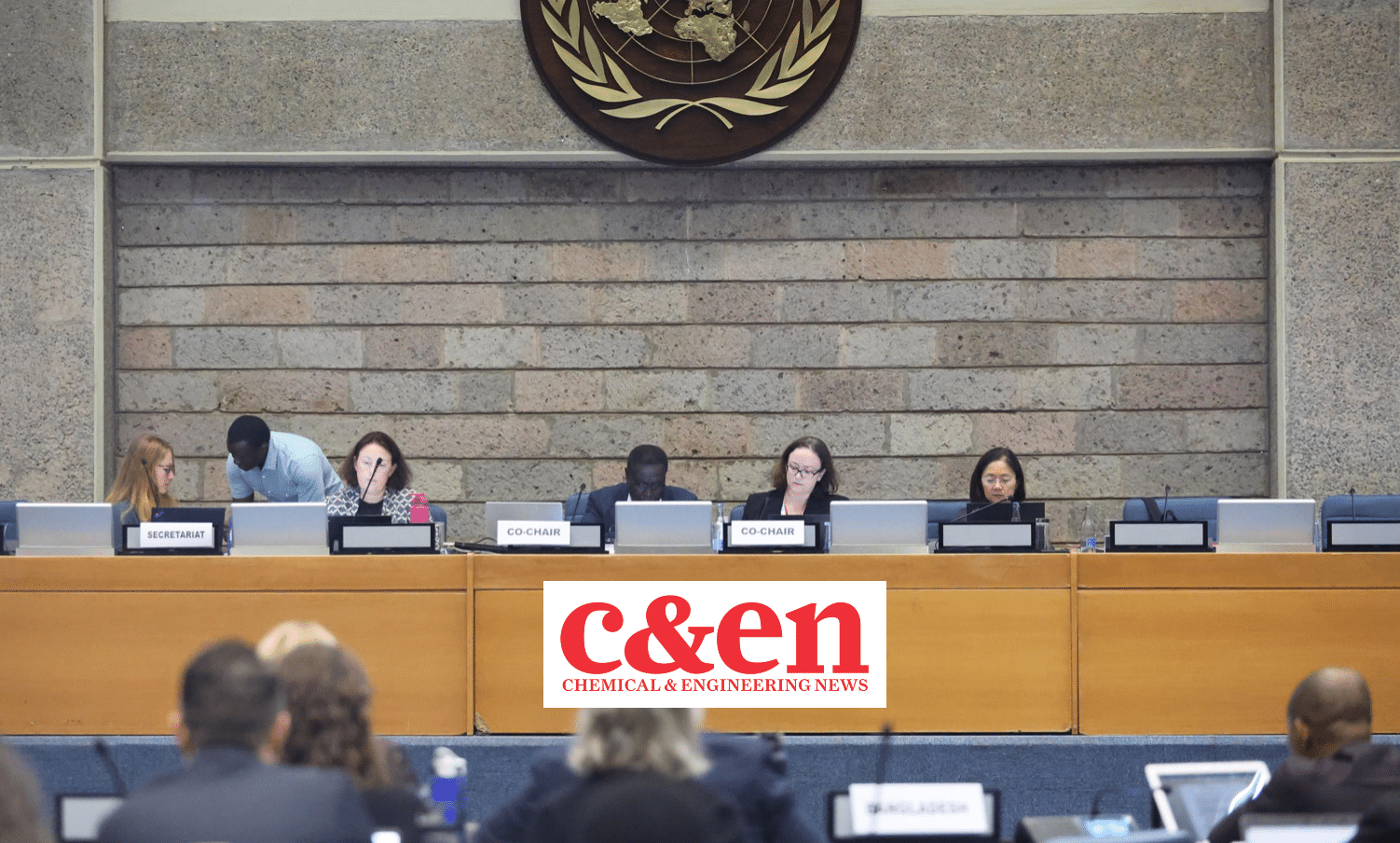 A panel of six people sit at a long table in front of a stone wall and a UN emblem, with C&EN Chemical & Engineering News displayed on the front. Audience members are visible in the foreground.