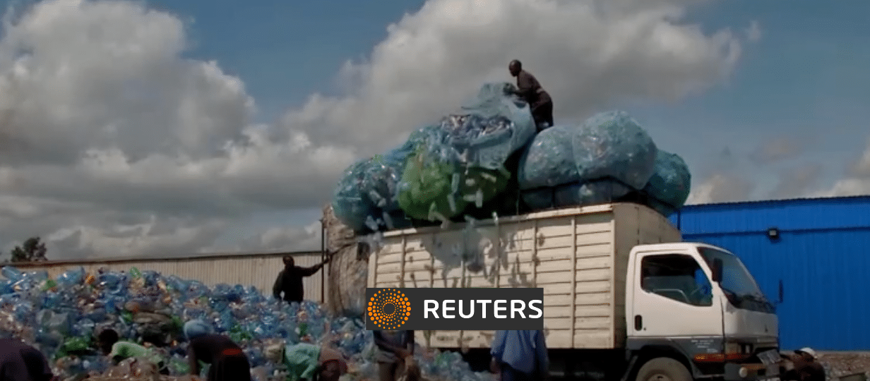 Several people load large bags filled with plastic bottles onto a white truck surrounded by piles of plastic waste, under a partly cloudy sky. The Reuters logo is displayed at the bottom center of the image.