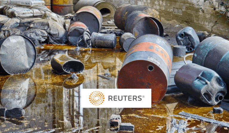 Rusty barrels and containers are scattered on the ground, leaking oily liquid. Worn sacks and industrial debris are visible in the background. A Reuters logo is overlaid on the image.