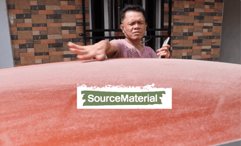 A person in a pink shirt uses their hand and a cloth to clean dust off the roof of a red car. The words “SourceMaterial” appear in green text on a white and green background over the car.