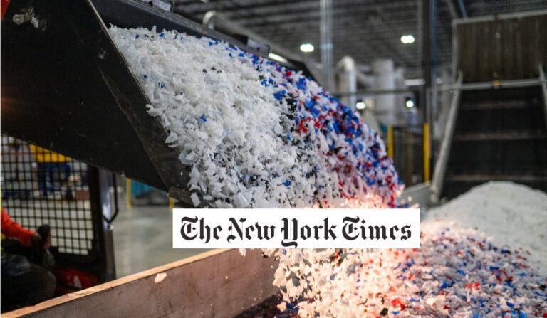 A conveyor belt releases a pile of shredded plastic pieces in white, blue, and red colors inside an industrial facility. The New York Times logo is centered on the image.