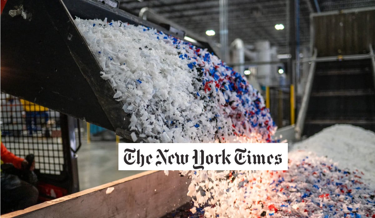 A conveyor belt releases a pile of shredded plastic pieces in white, blue, and red colors inside an industrial facility. The New York Times logo is centered on the image.