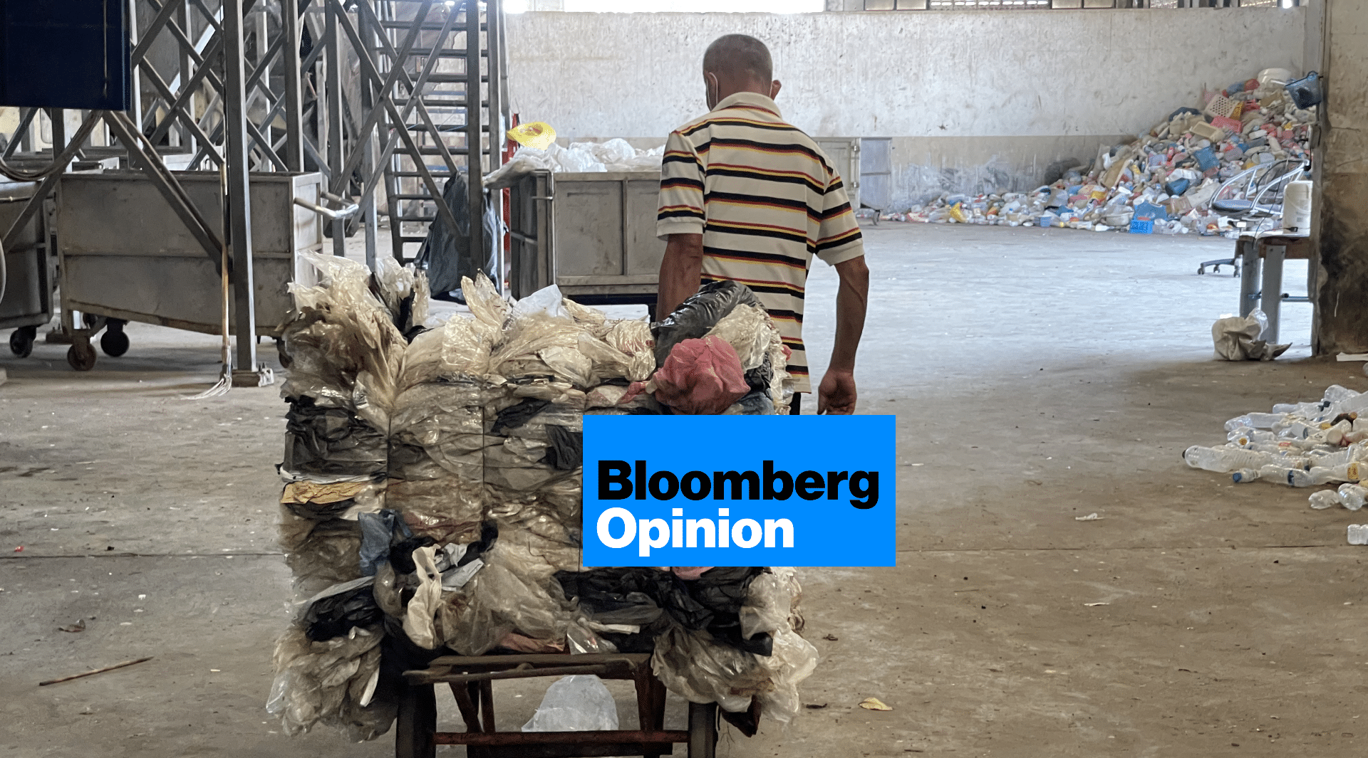 An older man wearing a striped shirt pushes a cart stacked with compressed plastic waste inside a large warehouse filled with scattered plastic debris. A Bloomberg Opinion graphic covers part of the cart.