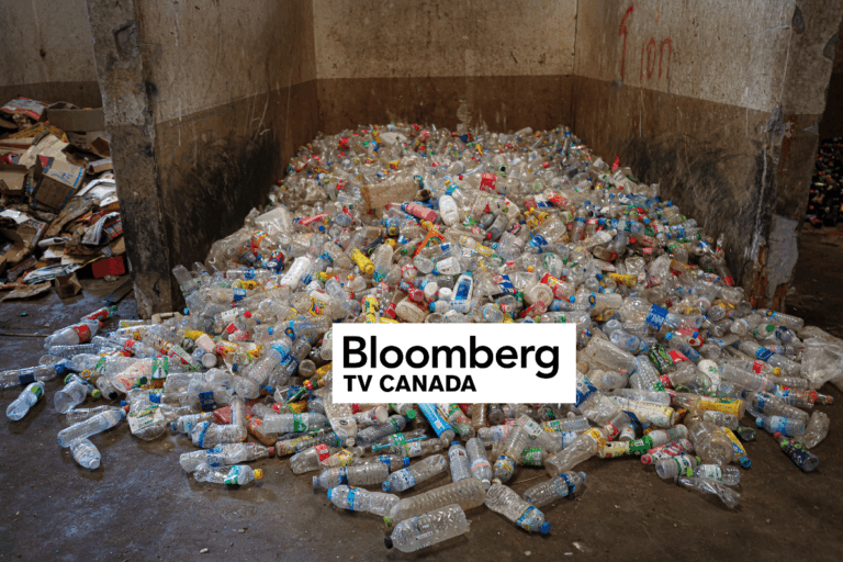 A large pile of empty plastic bottles covers the floor of a dirty, concrete room. Cardboard and more debris are seen in the background. A Bloomberg TV Canada logo is superimposed over the image.