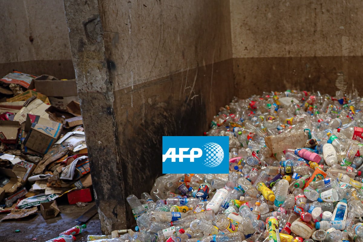 A pile of flattened cardboard boxes sits next to a large heap of empty plastic bottles in a dirty, indoor area. The AFP logo is superimposed on the image.