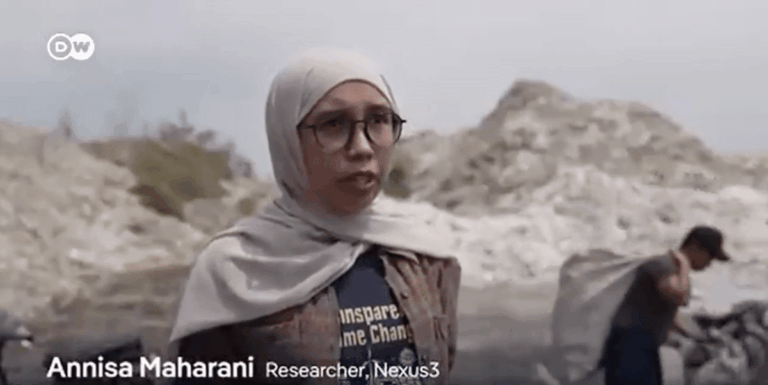 A woman wearing glasses and a headscarf stands outdoors in front of rocky terrain. Text on screen reads: Annisa Maharani, Researcher, Nexus3. Another person is visible in the blurred background.