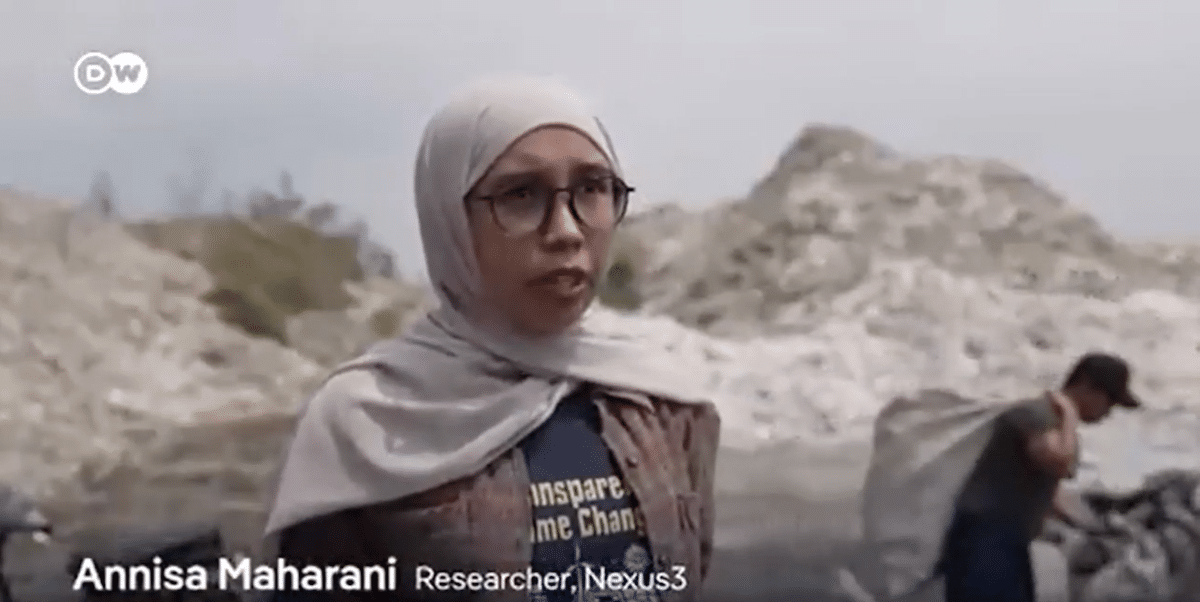 A woman wearing glasses and a headscarf stands outdoors in front of rocky terrain. Text on screen reads: Annisa Maharani, Researcher, Nexus3. Another person is visible in the blurred background.