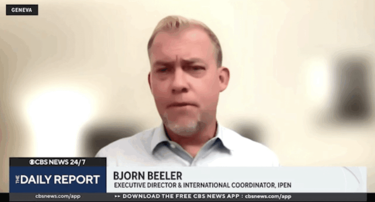 A man with short blond hair and a trimmed beard, wearing a light blue collared shirt, appears on a news broadcast titled The Daily Report. Text on the screen identifies him as Bjorn Beeler, Executive Director & International Coordinator, IPEN.