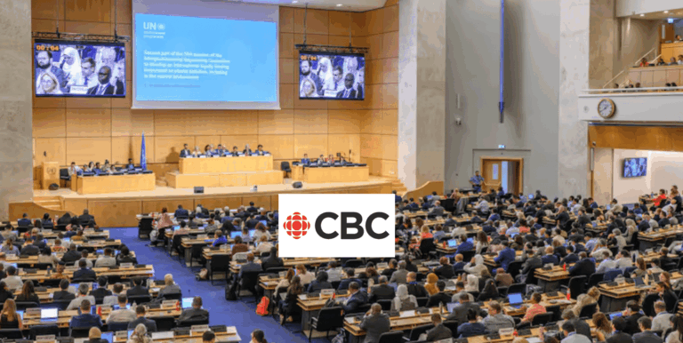 A large conference room is filled with attendees seated at rows of desks facing a stage with a panel of speakers. A large screen displays a UN presentation. The CBC logo is overlaid at the bottom center of the image.