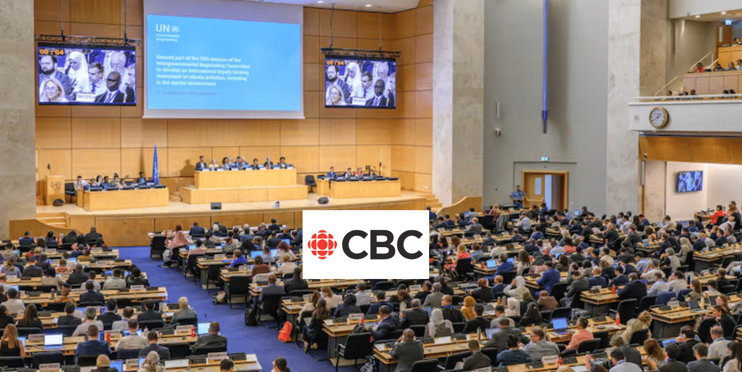 A large conference room is filled with attendees seated at rows of desks facing a stage with a panel of speakers. A large screen displays a UN presentation. The CBC logo is overlaid at the bottom center of the image.