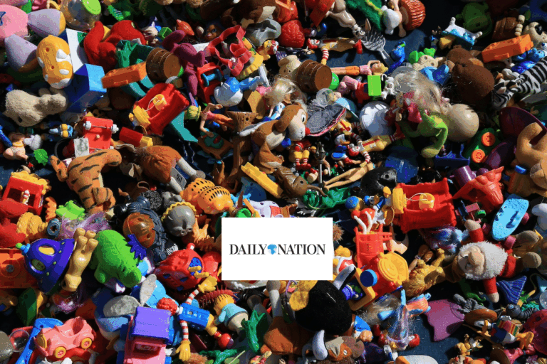 A large pile of assorted colorful plastic toys and figurines scattered closely together, with a white rectangular card in the center displaying the logo DAILY NATION.