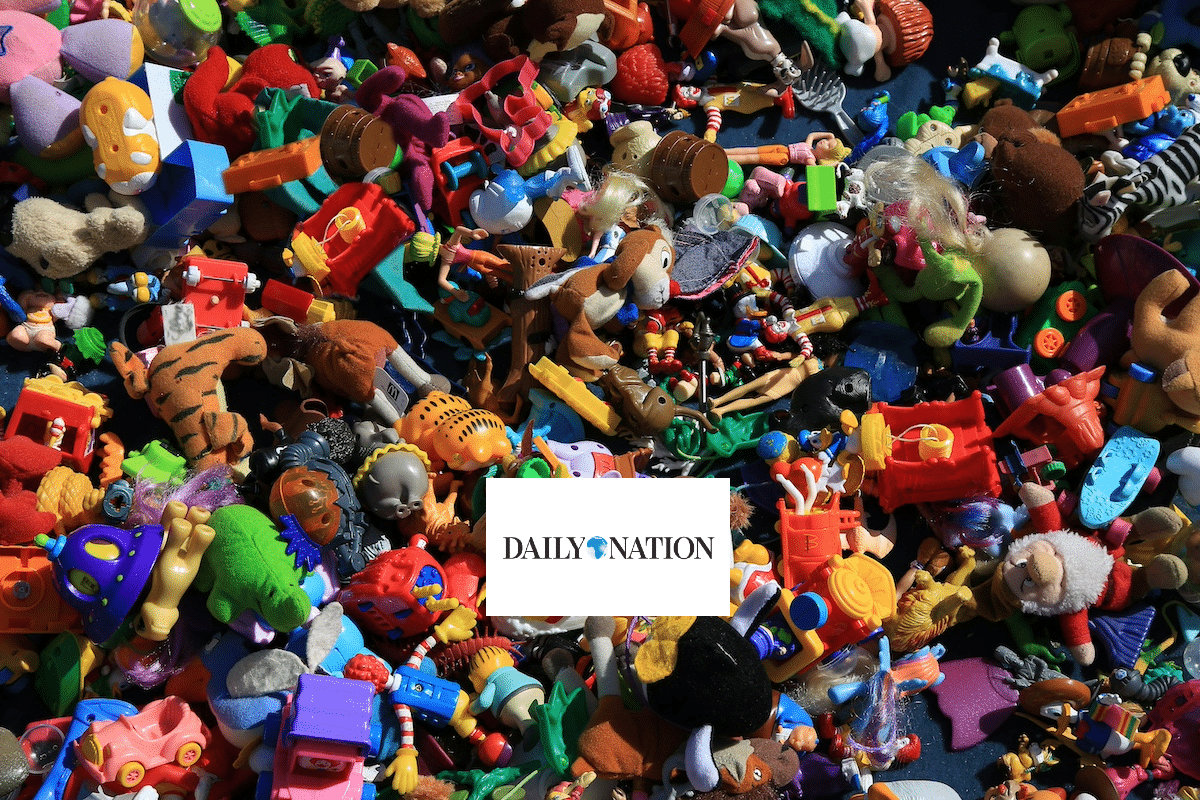 A large pile of assorted colorful plastic toys and figurines scattered closely together, with a white rectangular card in the center displaying the logo DAILY NATION.