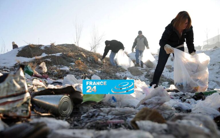 Several people pick up trash and litter with large plastic bags in a snowy outdoor area under a clear sky. The France 24 logo is overlaid on the image.