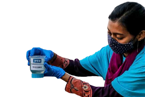 A person wearing a face mask and blue gloves holds a labeled container with both hands, examining it closely.