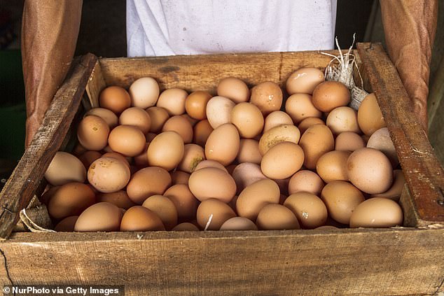 A person holds a large wooden crate filled with brown eggs.