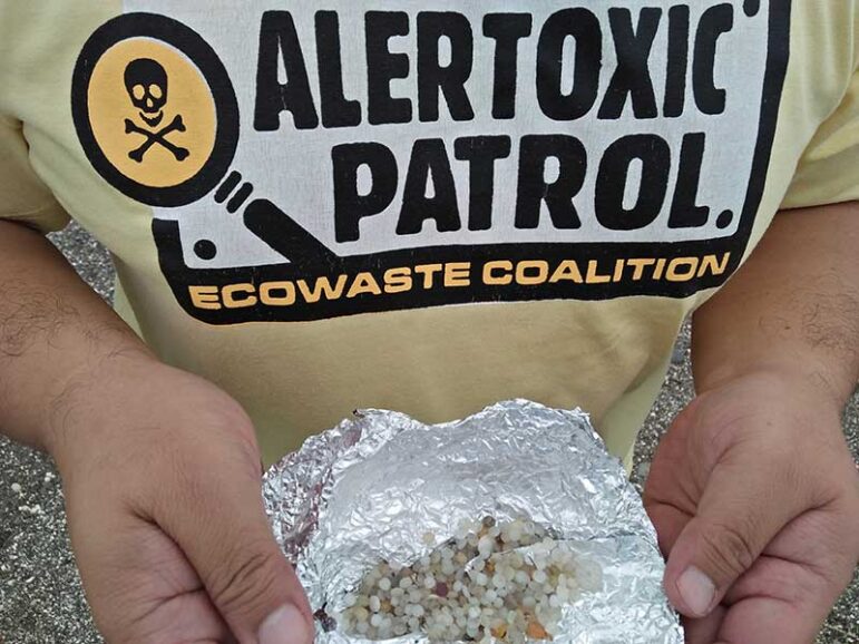 A person wearing a yellow shirt with the words ALERTOXIC PATROL ECOWASTE COALITION holds a piece of foil containing small plastic pellets or beads.