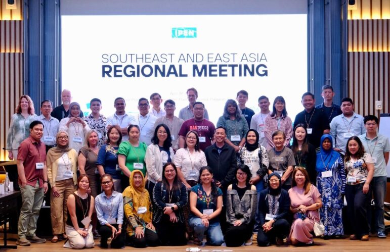 A group of about 40 people pose for a photo indoors in front of a large screen displaying the text Southeast and East Asia Regional Meeting. Most are smiling and facing the camera.