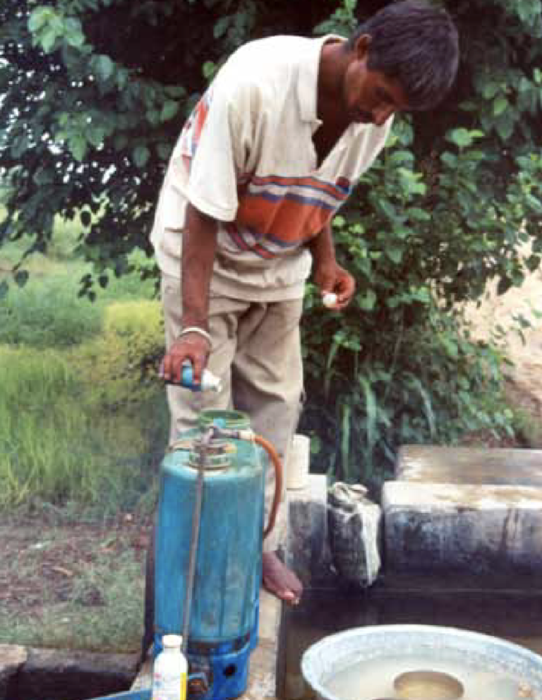 A barefoot man filling a bowl on the ground with pesticides