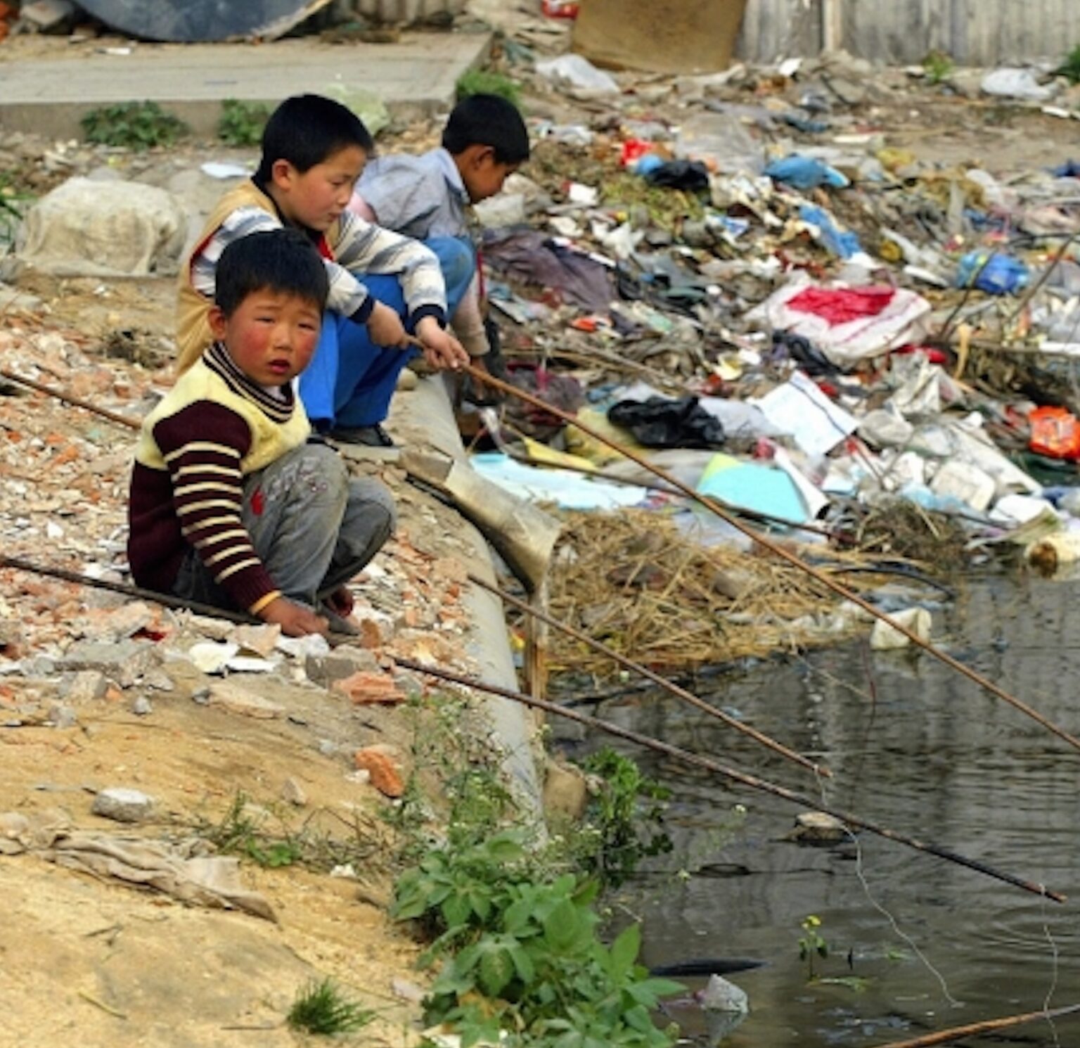 Boys sitting by a creek with plastic waste surrounding them on the banks