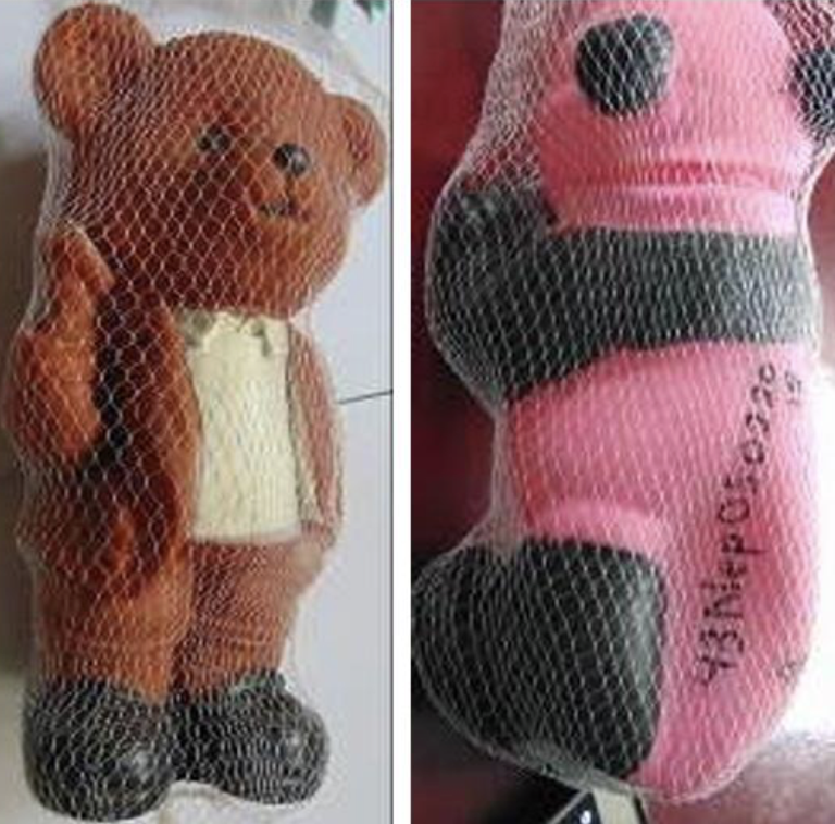 Two bear-shaped toys are shown side by side, each enclosed in white netting. The left bear is brown with a white chest and black shoes; the right bear is pink and black with writing visible on its side.