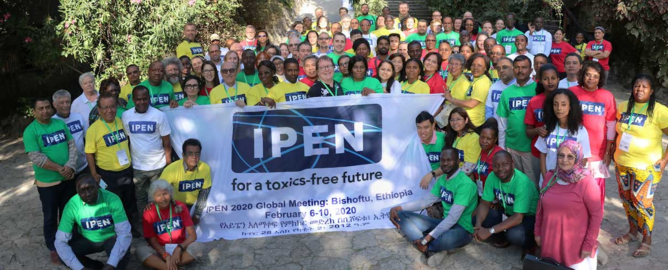 A large group of IPEN members outdoors holding a banner that reads “IPEN for a toxics-free future” at the IPEN 2020 Global Meeting in Bishoftu, Ethiopia. Many are wearing colorful IPEN T-shirts and facing the camera.