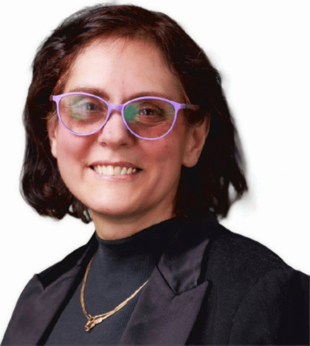 A person with short dark hair wearing light purple glasses, a black turtleneck, a black blazer, and a gold necklace, smiling at the camera against a white background.