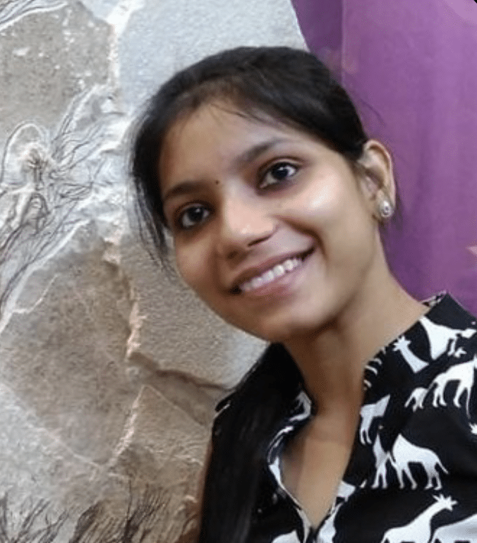 A woman with long dark hair, wearing a patterned shirt with white animal shapes, smiles at the camera. She is standing in front of a wall with a textured, abstract design.