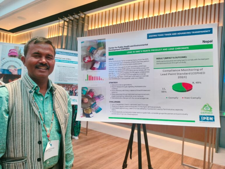 A man in a patterned vest stands beside a scientific poster presentation about compliance monitoring of lead paint standards in Nepal, displayed on a board at an indoor conference or event.