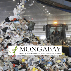 A large pile of mixed waste is being dumped in a recycling facility. A bulldozer is visible behind the pile, and an industrial conveyor belt is seen on the right. The Mongabay logo is overlaid on the image.