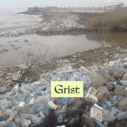 A shoreline covered with plastic bottles and trash, with water and a fence visible in the background. The word “Grist” appears in a highlighted box in the center foreground.